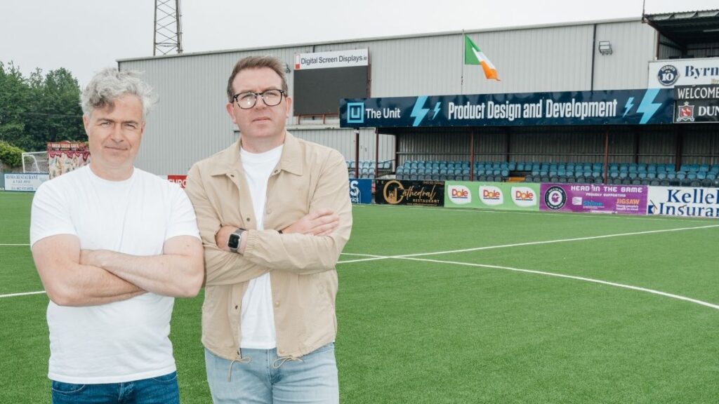 The Unit co-founders Conor Durnin and Paddy Casey at Oriel Park, with The Unit pitchside advertising behind them.